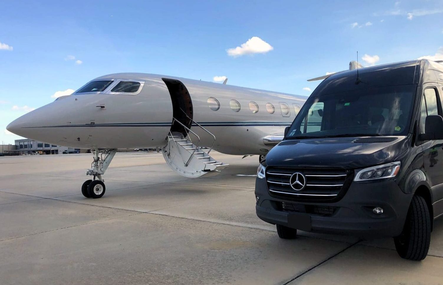A sleek black Mercedes Sprinter executive van parked next to a private jet on a sunny airport tarmac, showcasing Orlux’s seamless tarmac-side chauffeur services.