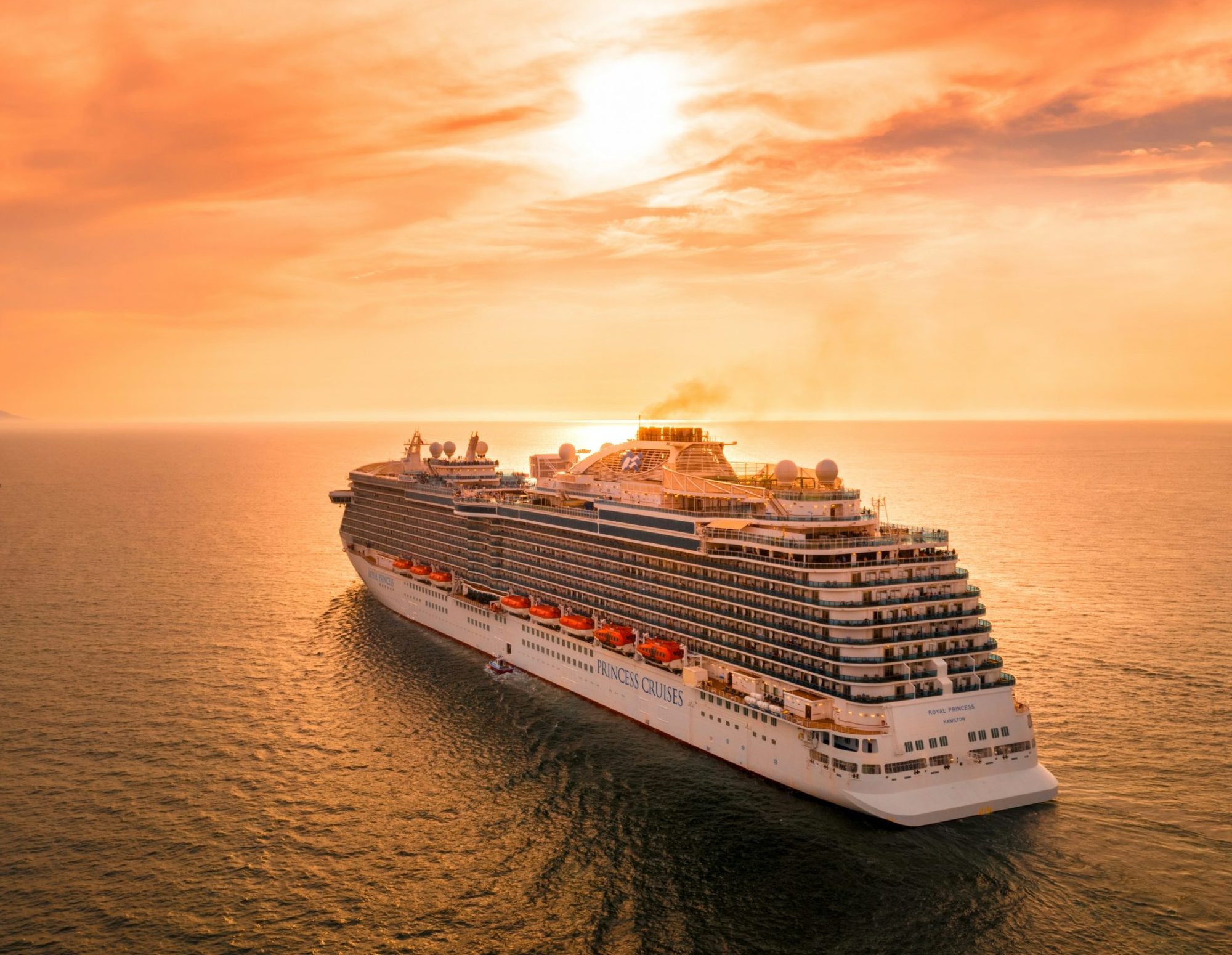 A massive white cruise ship with multiple decks and a red funnel docked at the Port Canaveral terminal under a bright blue sky.