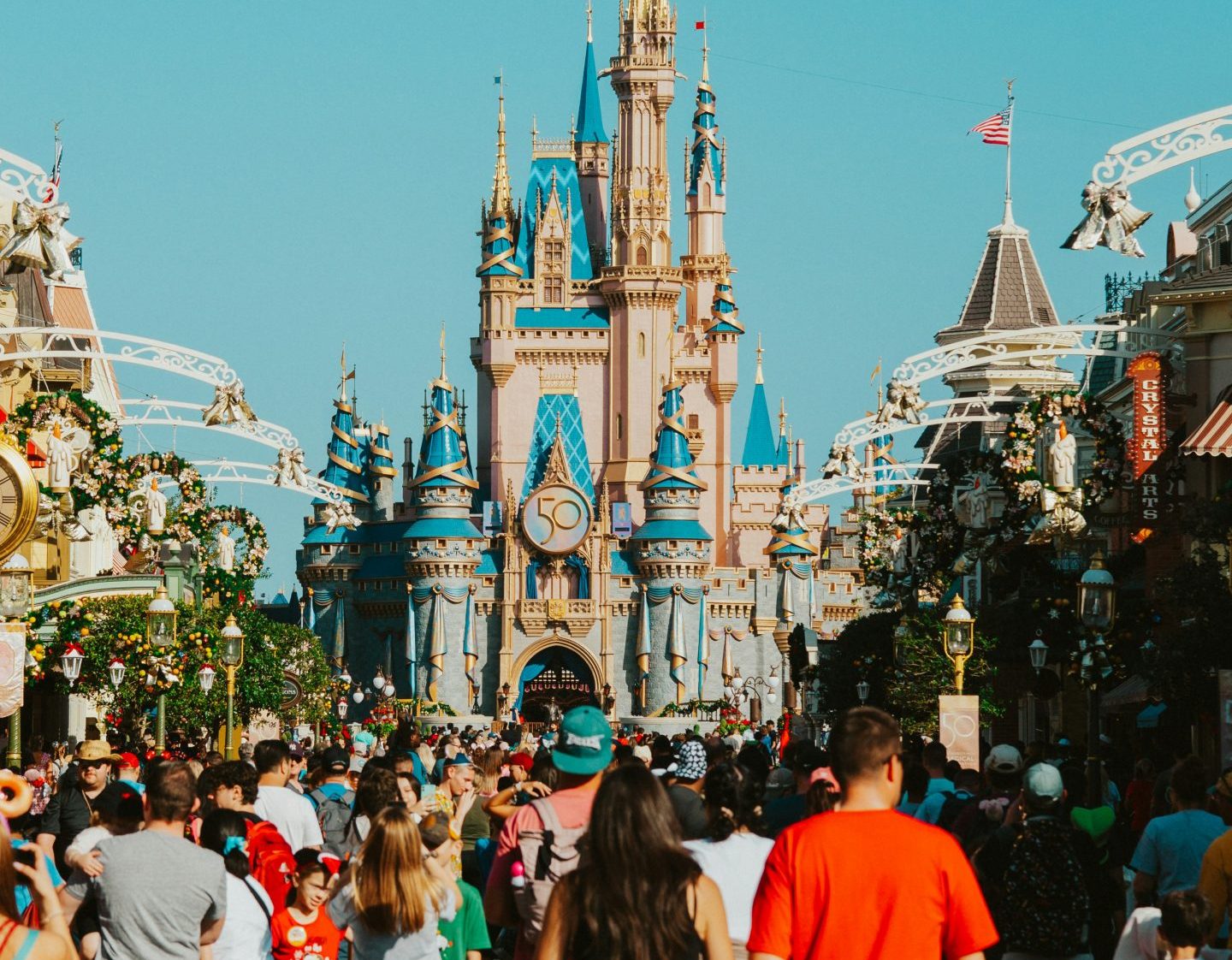 A crowded view of Main Street, U.S.A. leading toward Cinderella Castle at Disney World under a bright blue sky.