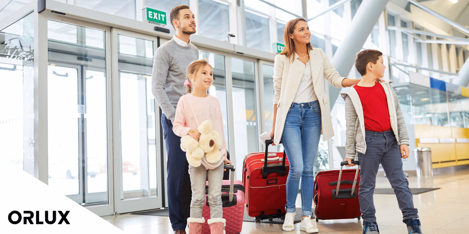 Family of four with red suitcases walking through an airport terminal