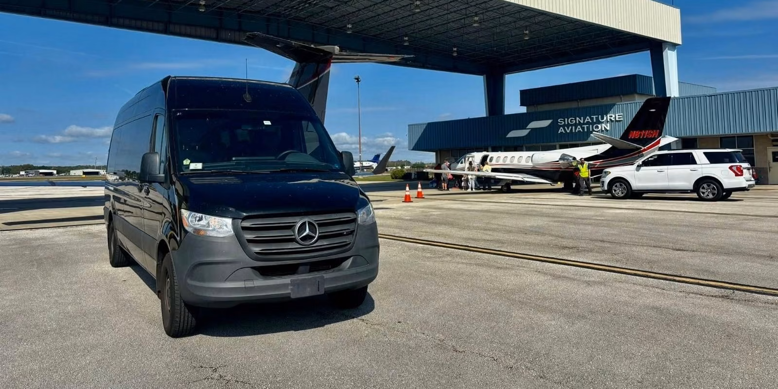 Black Mercedes-Benz Sprinter van parked on an airport apron outside a private-jet terminal