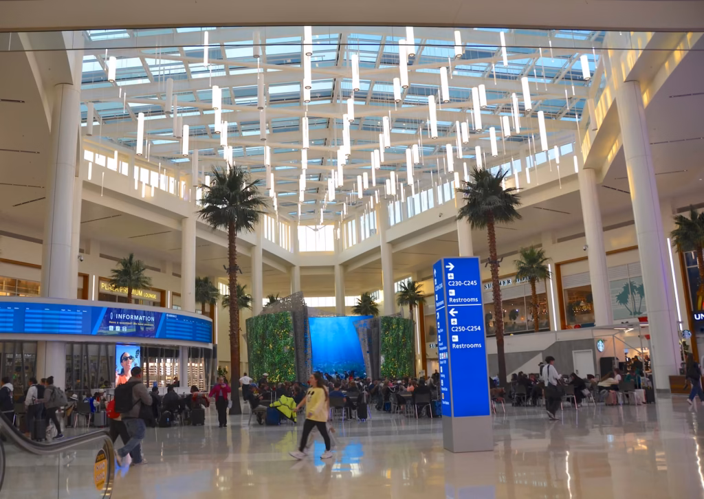 Terminal C hall at Orlando International Airport with palm trees and a blue sign to baggage claim and ground transportation